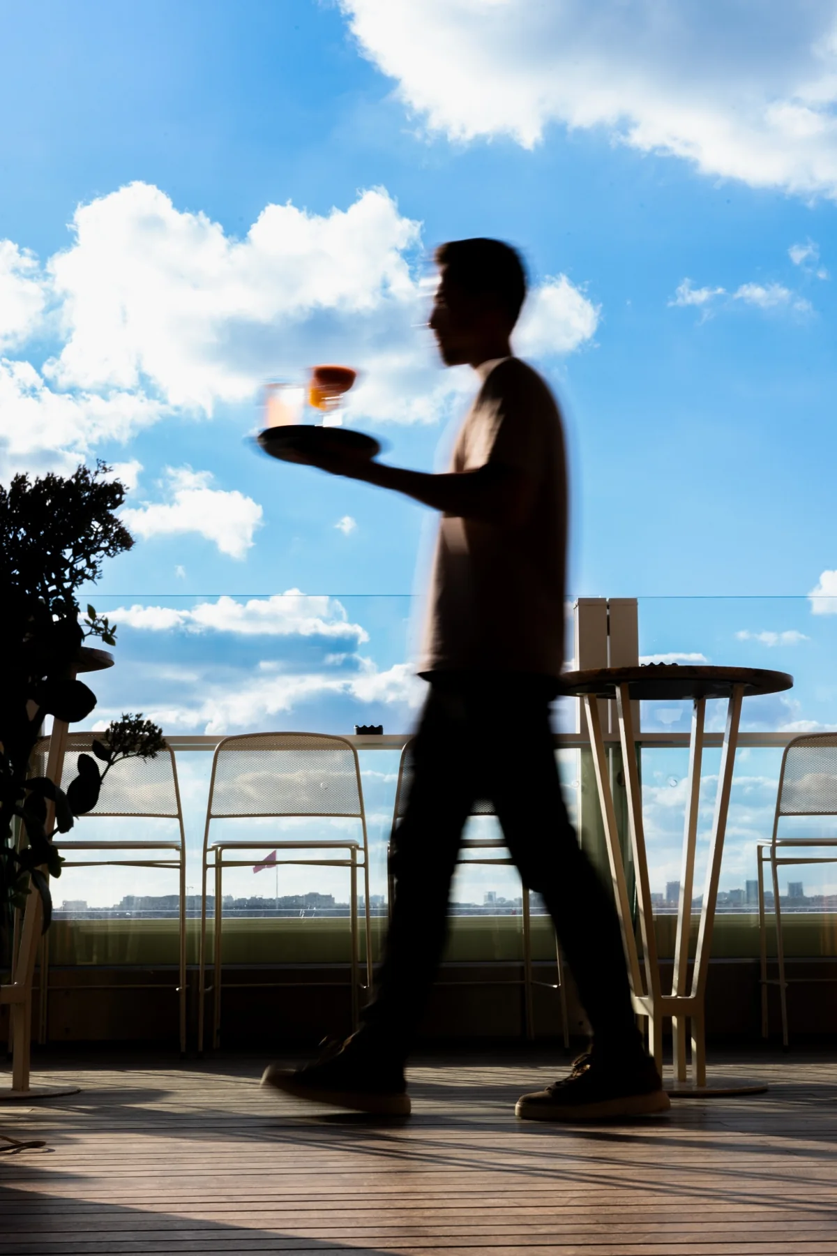 A server carrying cocktails across the rooftop against a blue sky